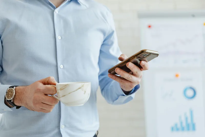 A business professional checking a smartphone while holding a coffee cup, representing the moment a creator monitors launch email performance