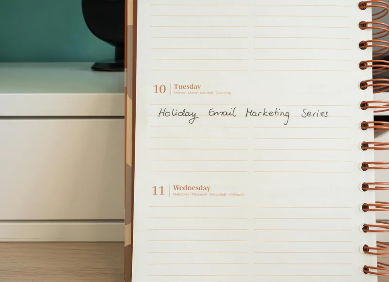 Open planner on a wooden desk showing handwritten email marketing series notes with a holiday email campaign schedule