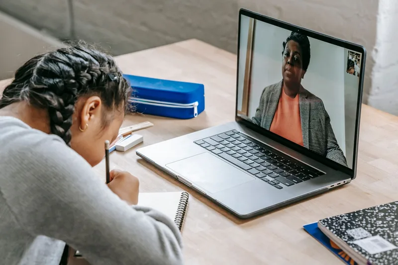Student watching an online lesson on laptop and taking notes in a notebook