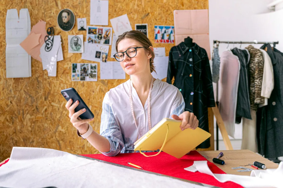 Creator sitting at a desk with a smartphone and notebook, working on a digital storefront