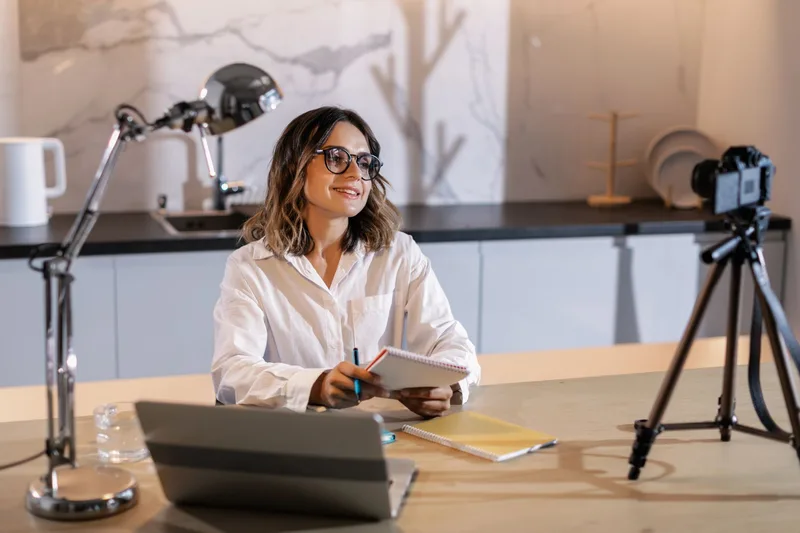 Woman creator at home studio, smiling while working with laptop and taking notes