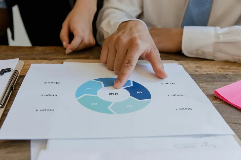 Hands pointing at a circular business strategy plan on paper, illustrating the decision-making process before choosing a funnel tool